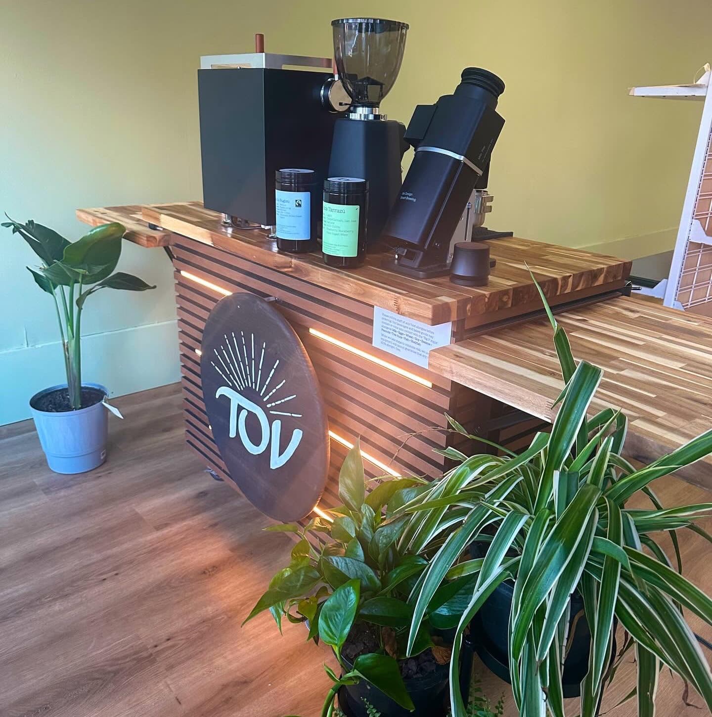 The Tov cart set up indoors: a slatted wooden counter lit from within, with an espresso machine, grinder and two jars of coffee on the butcher-block top.