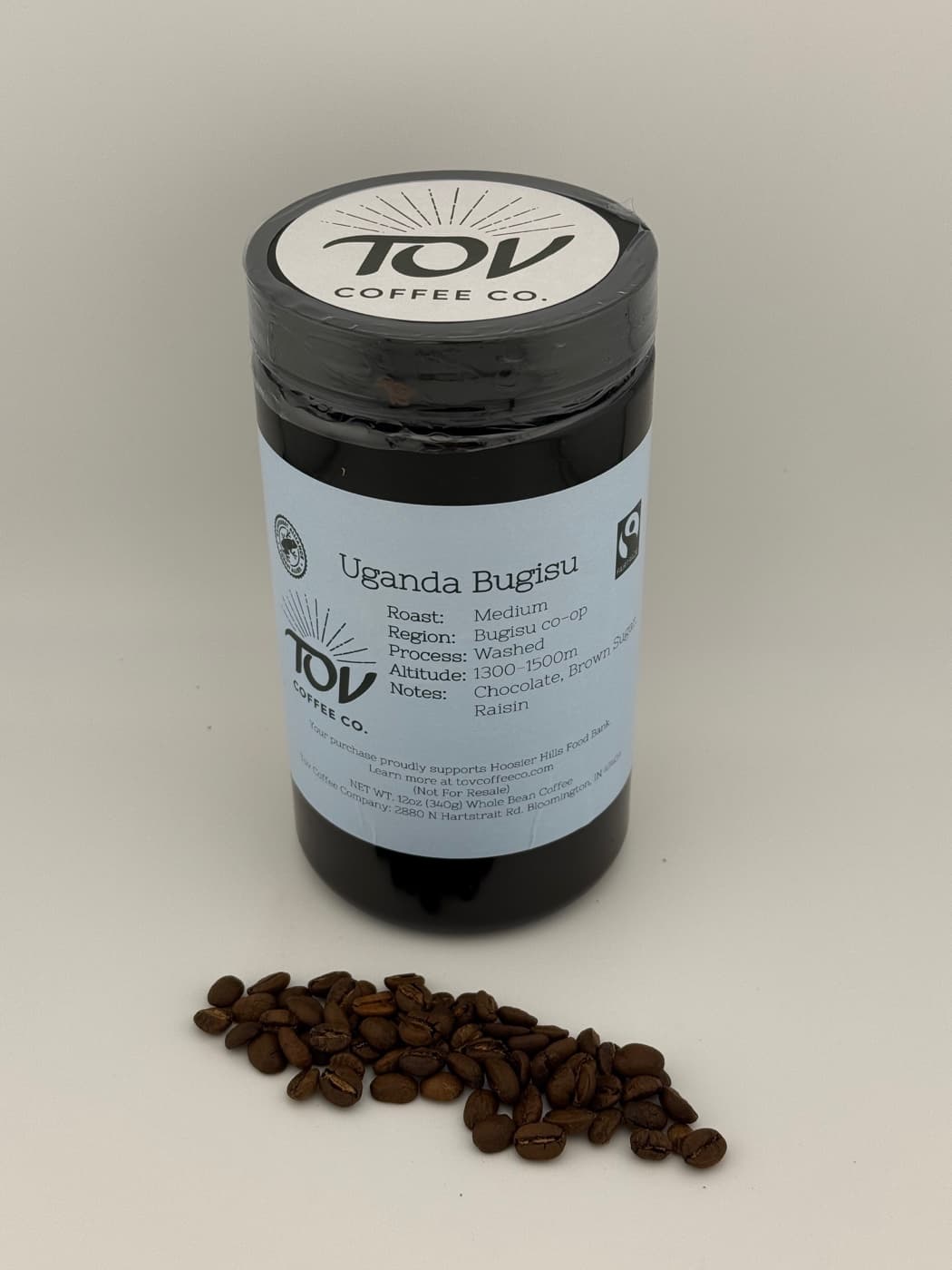 A 12oz jar of Tov Uganda Bugisu, with roasted beans beside it.